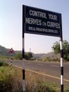 A rather humorous sign board advising drivers to control speed at a curve