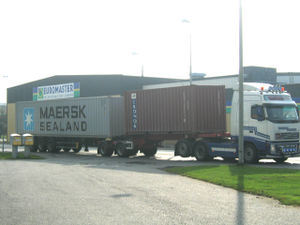 A truck with two trailers carrying one 20ft and one 40ft container.