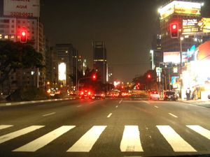 A picture of Avenida Faria Lima in So Paulo, Brazil, showing a semaphore-controlled pedestrian crossing, and several red lights on several intersections ahead.