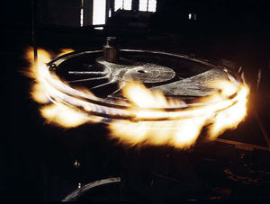 Steel tire on a steam locomotive's driving wheel is heated with gas flames to expand and loosen it so it may be removed and replaced.