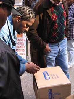 A shell game is performed with bottle caps on a cardboard box, on Fulton Street in New York City.