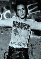 Johnny Rotten of the Sex Pistols, circa 1977, shows spiked and dyed hair, a deliberately offensive t-shirt featuring an inverted crucifix and Nazi swastika, a studded belt and tight leather pants.