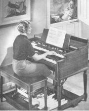  The classic Hammond electronic organ, invented in the 1930s and popular for decades thereafter. The Hammond brought an unprecedented degree of musical capacity into the home, far eclipsing the earlier reed organ. The organist here is making full use of those capabilities: as she plays on both manuals, her right foot, resting on the expression pedal, is in control of the volume, freeing her left foot to perform on the pedalboard. She has carefully adjusted Hammond's signature drawbars, which are clearly visible just above the upper manual.